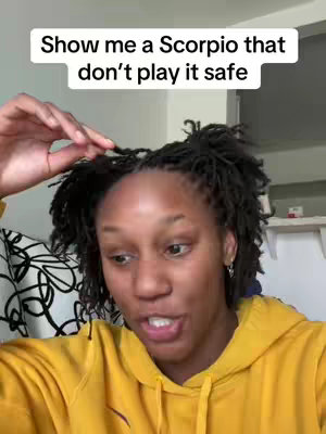 A person with medium-length dark hair in a yellow hoodie is looking at the camera and speaking. White text on a black rectangular background is present at the top of the image.