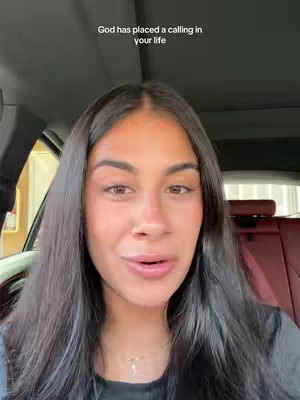 A woman with long black hair is seated inside a car, facing forward towards the camera. Soft lighting suggests the car is indoors, likely near a window.