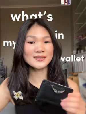 A woman with dark hair smiles and holds a black cardholder in front of a blurred background. The text overlay says, 'what's in my wallet'.