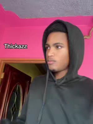 A young man wearing a black hoodie looks thoughtfully to the side. The background is a combination of a pink wall and an open doorway. The image is framed from the chest up, focusing on the man's face and upper body. The text overlay reads 'Thickazz'.