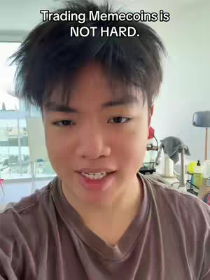 A young man is centered in the frame, looking directly at the camera and talking. The background is a softly lit room, with hints of furniture and equipment.  Text overlayed above is bold, reading 'Trading Memecoins is NOT HARD.'