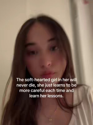 A close up video of a young woman, mostly from the chest up. The background is blurry and dark, while the woman is the main subject. The video has text overlayed on top of the video, written in a white font.