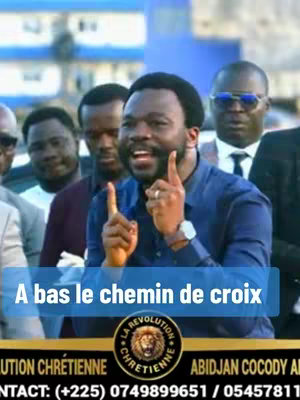 The cover image features a medium shot of a Black man with a beard and short hair, centered in the frame. He has a wide smile, and his index fingers are raised, pointing upward, with the background showing a group of men in suits. A text overlay in a blue rectangle reads, "A bas le chemin de croix". Below, a circular logo with a lion image and the words "LA REVOLUTION CHRETIENNE" is at the bottom, along with contact information.