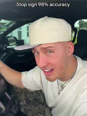 A man is sitting in the driver's seat of a car, looking at the camera with a surprised expression and open mouth. The overlay text says 'Stop sign 98% accuracy'.