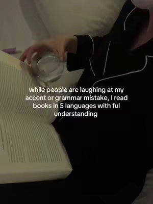 A low-angle shot inside a bedroom, showing a person in black pajamas holding a glass and reading a book. The book is open, with the pages visible, and the person's face is partially obscured. There is a pillow and a white blanket. Text overlayed on the image.