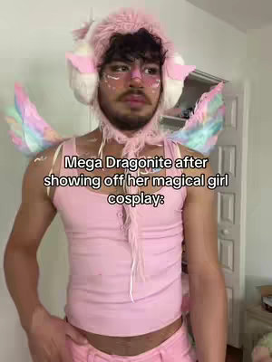 A person wearing a pink tank top, pink pants or shorts, and a pink hat with ear-like extensions and a matching scarf. The person has pink glitter on their face and is standing in a room. Text overlayed on the image reads, 'Mega Dragonite after showing off her magical girl cosplay:'