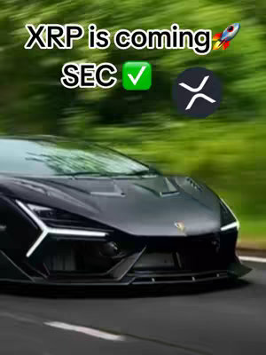 A black sports car is driving on a road, with a blurred green background suggesting a natural setting. The front end of the car dominates the frame.