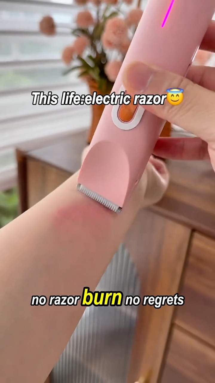 A person's wrist is shown with a pink electric razor gliding across it. Above the wrist, the skin is smooth, while a red patch indicates the area where the razor has been used. Text overlays read 'This life: electric razor' and 'no razor burn no regrets.' Against a blurred background of furniture and flowers.