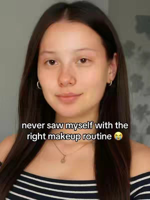 A woman with long dark hair and fair skin is centered in the frame, with text overlaid at the bottom that reads 'never saw myself with the right makeup routine'. She is wearing a striped top and a delicate necklace.