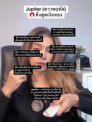 The image is a selfie-style shot of a woman against a blurred background, likely indoors. She is centered, with the framing from about mid-chest up. The woman has long, highlighted hair, is wearing subtle makeup, and is holding a white remote control in her right hand. The main focus is on her face, with several text boxes of information laid over the surface containing astrological information. The text is in Thai.