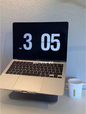 A laptop displaying a digital clock on its screen is positioned on a desk. A small white candle is placed beside the laptop. The background is a plain, light-colored wall. A text overlay is shown at the bottom of the image.