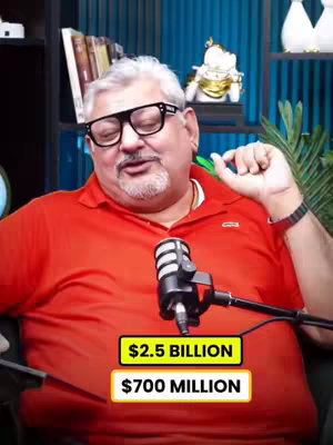 A man in a red shirt is speaking while holding a microphone. Overlaid on the bottom of the image are two yellow rectangles, one stating '$2.5 BILLION' and the other '$700 MILLION'. The background has plants and shelves.