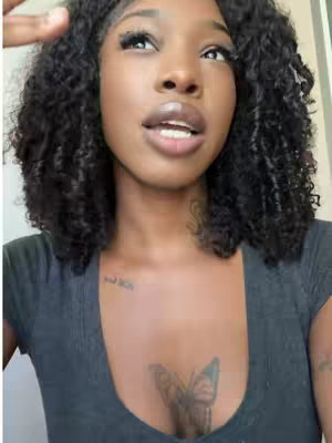 The cover image features a close-up of a woman with dark, curly hair. She has full lips, and her eyes are looking upwards. The woman wears a gray top, and a butterfly tattoo is visible on her upper chest. The background is a simple, neutral color.