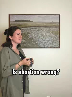 A woman is standing in front of a wall with a painting. The woman is holding a mug and looking to the side. Overlay text reads 'Is abortion wrong?'.