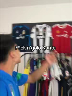 A person wearing a blue jersey with the Italian flag on it, is facing to the left side of the image, the arm on the right is raised, looking in the same direction. Behind the person are a rack of different soccer jerseys on display. Above the person is text overlayed in white on the image. 