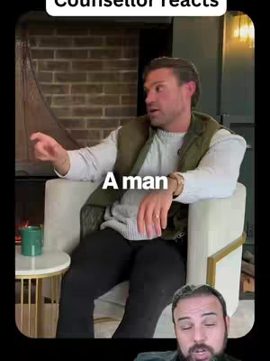 The image shows a man seated on a cream-colored armchair, positioned in front of a brick fireplace. He's gesturing with his right hand as he speaks, wearing a white sweater, a green vest, and black pants. Overlayed at the bottom right there is a cropped headshot of another man who is also speaking. The text overlay "A man" is placed over the main figure's body.