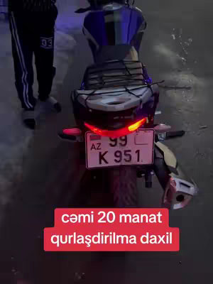 The cover image shows the rear view of a black and blue motorcycle parked on a dimly lit street. The motorcycle's tail lights are illuminated. A person, whose legs are visible, is standing nearby the bike. Text overlaid on a red bar at the bottom of the image advertises a price.