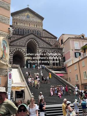 A large church with a detailed facade and stairs. People are walking up the steps and in front of the church. The sky is blue and the overall aesthetic is bright and sunny.