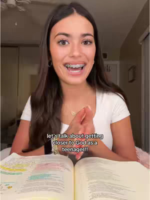 A young woman with long dark hair and braces is smiling, holding a bible in front of an open book, while the text "let's talk about getting closer to God as a teenager!!" is overlaid on the bottom.
