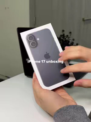 The cover image shows a person holding a black iPhone in its white box. The phone has a dual-camera setup and an Apple logo on the back. The person's hands are visible, holding the box against a white background with a dark object partially visible in the background.
