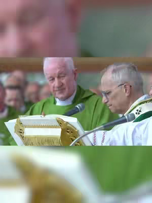 The image shows two men in religious attire. One, wearing a green garment, is facing forward, looking down at a book or lectern. The other, in white and green, is looking down to his right, with a microphone in front of him. The background features blurred figures.