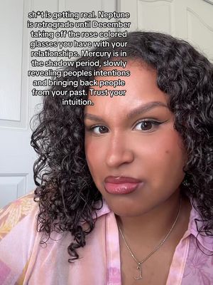 A close-up selfie of a woman with curly hair and makeup. Text is overlaid in black. The background is a plain wall.