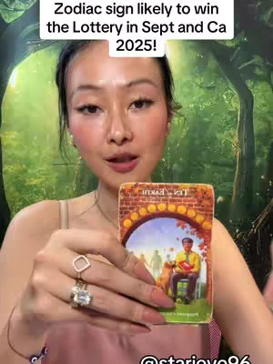 The cover image features a young woman holding up a tarot card. She is centered in the frame, with a blurred green forest background. The text overlay at the top reads "Zodiac sign likely to win the Lottery in Sept and Ca 2025!". She is wearing a light pink top and has several rings on her fingers.