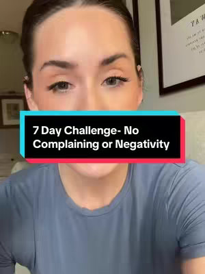 A woman in a blue shirt is centered in the frame, looking at the camera. A text overlay in a black box with a blue and red stripe across the top partially covers the woman's lower face. The text states, "7 Day Challenge- No Complaining or Negativity."