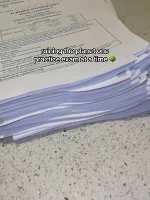 A stack of printed practice exams on a light-colored countertop. The text overlay humorously suggests environmental impact.