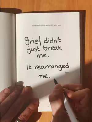 An open book with a white page is shown. Handwritten sentences are written on the page that express personal feelings, with a hand holding a marker in the frame. The background is wooden, adding warmth to the scene.
