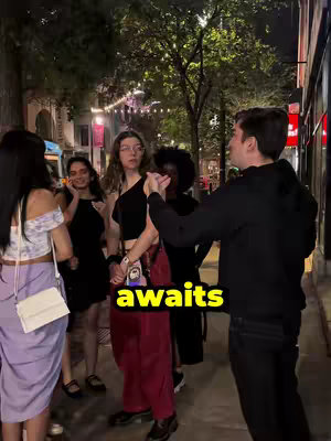 The cover image shows a nighttime street scene with several people. A group of about six individuals stands in a line along a building. A man in a black hoodie is speaking to someone just off-camera. The text overlay is a rectangle to indicate 'awaits'. The background features ambient lighting from streetlights and storefronts, creating a casual yet populated ambiance.