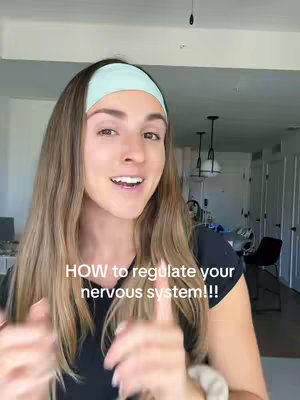 A woman with long brown hair and a light blue headband is centered in the frame, smiling and gesturing with her hands. The background subtly reveals a domestic interior suggesting a bright, airy atmosphere. Overlayed text in white font reads 'HOW to regulate your nervous system!!!'.