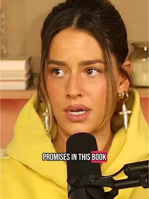 A woman with dark hair and a yellow hoodie is speaking into a microphone. A text overlay saying 'PROMISES IN THIS BOOK' is also visible.