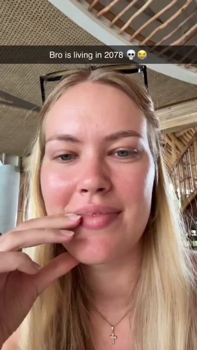 The cover image features a close-up selfie of a woman with long blonde hair and a light complexion. She's wearing a necklace. She's holding a finger near her lips, with a slight, thoughtful smile. Behind her is a blurred background suggesting an outdoor setting with wooden and woven textures.