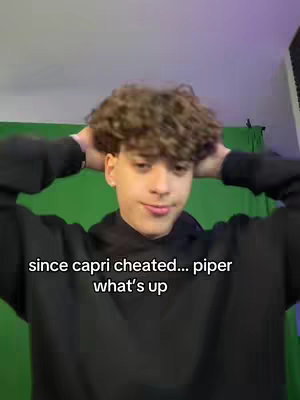 A young man with curly brown hair poses with his hands behind his head, smiling softly. He wears a black hoodie set against a solid green background, and the overlayed text is white and easy to read.