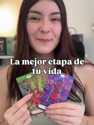 A woman is holding two tarot cards in front of her, smiling at the camera. Text overlayed says "La mejor etapa de tu vida".