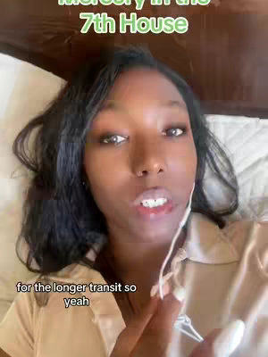 A woman is lying in bed, looking at the camera, with text overlay in green in the top part of the screen. There is text in the bottom area of the screen as well. She is wearing a tan colored shirt.