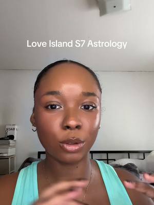 A person with dark hair and wearing a teal top looks directly at the camera in a close-up shot. The background is a simple white or off-white wall and ceiling, with a corner of a room visible in the background. At the top center of the frame, there is white text overlayed that reads, "Love Island S7 Astrology".