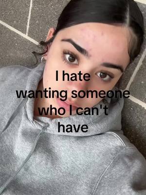 The cover image presents a selfie taken from a slightly above angle, featuring a person in a gray hoodie against a patterned background. The person's face is the central focus, with text overlayed that reads "I hate wanting someone who I can't have". They look directly at the camera with a neutral expression.