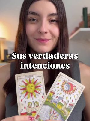 A woman with long brown hair is holding two tarot cards in front of her, with the text "Sus verdaderas intenciones" (Her true intentions) overlaid. The background is blurred, suggesting an indoor setting, and the woman is smiling. The color palette is warm, with the tarot cards featuring yellow and blue.