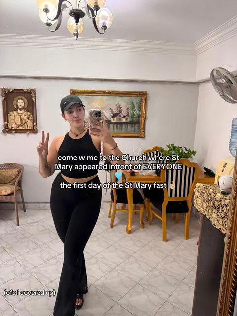 A selfie video showing a woman posing in a room with a mirror, and a religious painting on the wall.