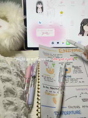 A close-up shot showcasing a study setup. In the foreground are pens, study notes with diagrams, and a notebook. A tablet with a pink cloud background sits in the midground, and white, fluffy fabric is in the left of the frame.