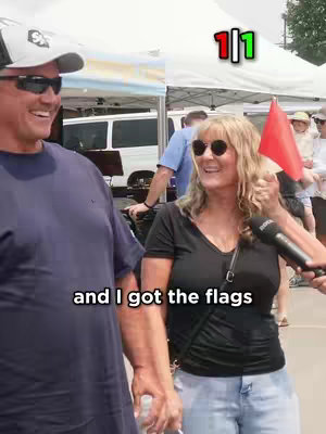The cover features two people, a man and a woman. The man on the left is wearing sunglasses, a white baseball cap, and a dark blue shirt. The woman is wearing sunglasses and a black V-neck shirt. She is holding a red flag. The background shows an outdoor setting with tents and people.