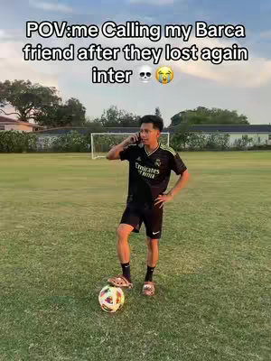 A young man stands on a green soccer field, holding a cell phone to his ear, and the soccer ball is at his feet. Above him is text with the skull and crying emoji, with the sky and buildings in the background.