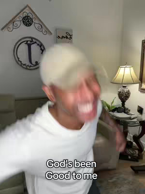 A blurry image of a man indoors with a white cap and white shirt, his mouth open and eyes slightly blurred. The scene is blurry, emphasizing action. Below him, text overlays the words "God's been Good to me".