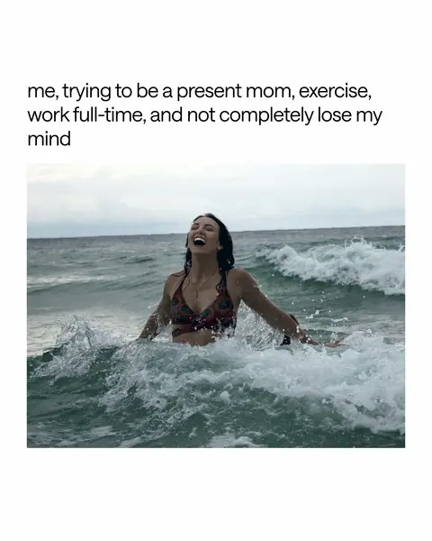 A woman in a patterned bikini top is laughing with her arms outstretched in the ocean, surrounded by splashing water.