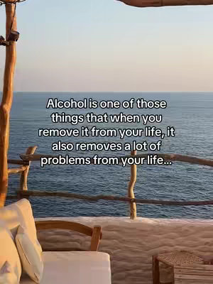 A serene outdoor scene features a wooden structure with a white cushion and pillow in the foreground. Beyond the structure, the vast, calm ocean extends to the horizon under a clear sky. Text overlays provide a message about removing alcohol.