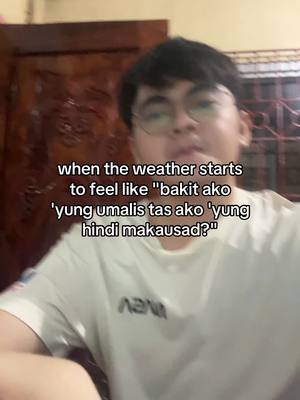 A young man with short, dark hair and glasses gazes directly at the camera. He's wearing a white t-shirt with a small logo, and the background includes a wooden door and window with curtains. Text overlays relate to weather and feelings.