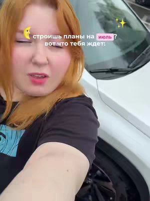 A selfie-style image with a fair-skinned woman with red hair as the primary subject. She's positioned in the foreground, with a close-up focus on her face. Her gaze is directed slightly off-camera, and her expression is a mix of surprise and perhaps a slight wince. Her face is framed by her ginger hair, she is wearing a black shirt, and the background shows the side of a white car and some greenery.
