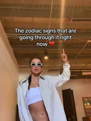 A woman in white sunglasses and a white crop top and unbuttoned white shirt points up with a middle finger. Text is overlaid on the image.